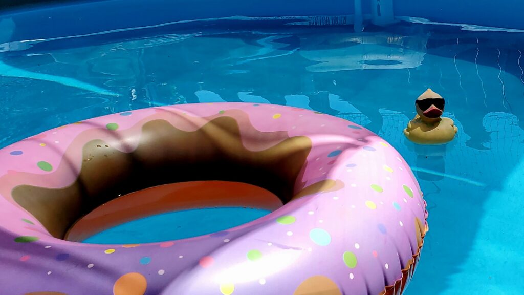 Image of pink plastic inner tube and plastic duck floating in swimming pool